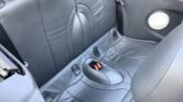 The image shows the back seat of a MINI, upholstered in black leather. The seat features modern stitching patterns and includes seatbelt buckles. The car door is partly visible with a round speaker embedded into it. The overall appearance is clean and well-maintained.