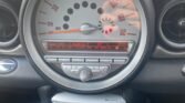 A car dashboard in a 2006 Mini Cooper showing a speedometer with a range up to 150 mph and a central radio display currently tuned to "1 Radio 1." Below the radio are various controls for the climate and entertainment systems. The Turbo R56 model also features a sleek black interior with chrome accents and a pan roof.