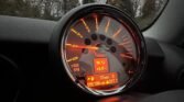 A modern car tachometer with an illuminated digital display, reminiscent of the 2008 Mini Cooper. The tachometer's needle points to 1.2 (x1000 RPM). The digital screen shows the time (16:12), temperature (5.0°C), and distance traveled (37 miles). The total trip and odometer readings are also visible in orange-red lighting.