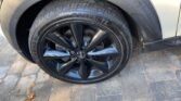 Close-up of a 2013 MINI Hatchback's front left tire and black alloy wheel on a paved surface. The car, a light-colored Cooper 3dr, features Nokian tires with "Nokian" visibly marked on the sidewall. The wheel boasts a glossy finish and five spokes, with some fallen leaves scattered on the pavement.