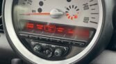 Close-up of a MINI car dashboard featuring a large, circular speedometer centrally located, marked up to 160 MPH. Below the speedometer are displays showing options for Tuner, DAB, Insert CD, AUX, USB. Additional controls for audio and climate control are visible beneath the displays.