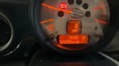 A close-up view of a MINI car dashboard displays a tachometer with orange backlighting. The dial shows an RPM reading up to 8,000 with a needle pointing at zero. The digital display underneath shows the time as 12:04 and the mileage as 131393 miles. The speedometer reads 0 mph.