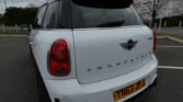 Rear view of a white MINI Countryman parked in an empty lot. The car's back features the distinctive MINI logo and 'Countryman' branding. It has a license plate with registration 'YN63 JPJ.' The taillights are red, and the sky is overcast with bare trees in the background.