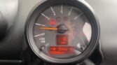 Close-up view of a MINI's speedometer and odometer inside the dashboard. The speedometer needle is at 0 mph, and the odometer shows 69,666 miles. The trip meter displays "123 miles." Multiple warning lights are illuminated, including the handbrake and engine check lights.