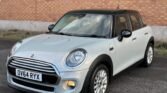 A silver 5-door Mini Cooper with a black roof is parked on a paved surface in front of a brick wall. The car has a UK license plate "OV64 RYX." This diesel vehicle features rounded headlights, chrome accents, and slightly tinted windows.