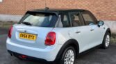 A white Mini Cooper Diesel hatchback with a black roof is parked on an asphalt surface near a brick wall. The car has a UK license plate reading "OV64 RYX". This 5-Door vehicle features red tail lights and silver alloy wheels, with the rear and left side of the car visible in the image.