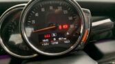 A MINI car dashboard displays a speedometer, odometer, fuel gauge, and various warning lights. The speedometer reads zero. The digital screen shows a time of 16:43, temperature of 5°C, "N" for neutral, mileage of 12758 miles, trip distance of 142.3 miles, and an average fuel economy of 40.7 mpg.
