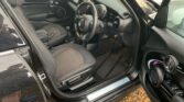 Interior view of a black MINI with the driver's door open. The seats are dark gray with a textured finish. The dashboard and steering wheel showcase a modern design with various controls and displays. The car door has a sleek inner panel highlighted by purple ambient lighting accents.