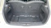 An open MINI car trunk with the rear seats in the upright position. The trunk is empty, featuring a black rubber cargo mat with a dotted texture. The interior is clean and there are two small handles or locks on the backside of the rear seats.