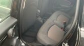 A black MINI's rear passenger seats are shown from the open door. The upholstery is dark grey with black trim, and there are red seatbelt latches. The door panel features subtle ambient lighting. In the background, rain droplets are visible on the window outside the car.