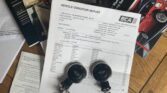 A wooden surface holds documents and two car key fobs with the MINI logo. Visible papers include a vehicle condition report from BCA, owner's handbooks, and several other booklets with images of MINI cars. A smaller piece of handwritten paper is also partially visible on the left.
