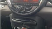 Close-up of a MINI car dashboard with a large, analog speedometer in the center, showing a white background and numbers in black. Below it is a digital display showing the time as 11:37 and the date as 03-09-26. Below this are various buttons and knobs, including climate control settings.