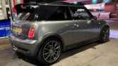 A grey MINI Cooper with black-tinted windows and custom black rims is parked at a gas station. The station is lit with overhead lights, and LED signs can be seen in the background. It's nighttime, evident by the dark sky and artificial lighting. The license plate reads "YA54 JFA".