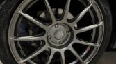 A close-up view of a car's wheel, featuring a metallic alloy rim with multiple spokes in a star pattern. The rim has a central cap with the RH logo. The tire, marked with the Hankook brand, has a visible tread and is mounted on a dark-colored MINI parked on a concrete surface.