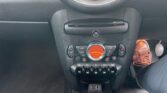 The image shows the center console of a MINI Cooper car, featuring the climate control system and other controls. The display shows a temperature setting of 25°C. A driver's foot, wearing a brown shoe, is visible to the right near the car's gas pedal. The console also has cup holders and a USB port.