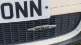 Close-up view of the front grille of a MINI with a white license plate displaying partial letters "ONN". The middle of the grille features a "John Cooper Works" emblem. The surrounding area of the grille is white with a black lower edge.