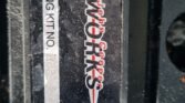 Close-up of a black metal part with a "John Cooper Works" logo in red and white, indicating it's for a MINI. Below the logo is a label that reads, "TUNING KIT NO R56JCW10686," specifying the tuning kit number. A coiled cable is visible in the bottom part of the image.