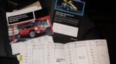 A collection of car-related documents, including a MINI service booklet, an owner's manual, and a warranty handbook, laid out on a car seat. Each document is open, showing detailed service records with stamps and signatures, along with a flyer featuring a vibrant yellow MINI.