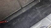 A grey, carpeted car trunk in a MINI with the rear seats upright. The trunk is clean and empty, with a visible latch mechanism at the bottom. Some small details of the car's side walls and interior lining are also visible, contributing to a well-maintained appearance.