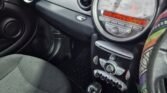 Interior of a Mini 2007 showing the dashboard and front seats. The steering wheel, partially visible and covered with a colorful patterned cover, is on the right. The dashboard includes a central speedometer with an electronic display and various controls. The automatic gear shift is also visible in the center console.