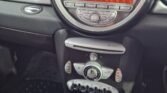 Dashboard view of a 2007 Mini car interior featuring a large, circular speedometer that reads 60 MPH. Below it is a digital screen displaying "Radio 1" and the time, 12:24. The dashboard also includes various buttons and climate control knobs. The automatic gear stick and cup holders are visible at the bottom.