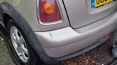 A close-up image of the rear end of a silver 2007 Mini Cooper during a rainy day. The car has a British registration plate starting with "GU07." It is parked on a wet street with a hose seen on the ground near the car, suggesting it is being washed or cleaned. The car's paint is shiny, reflecting raindrops.