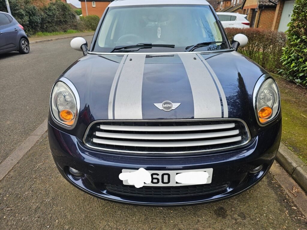 This Mini Countryman Cooper D 1.6 is a 5-door hatchback with Cosmic Blue exterior & silver stripes with a White Roof and Silver roof rails.Interior is black with grey cloth seats and a centre rail which holds a mini glasses case