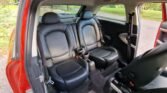 The image shows the interior of a MINI, specifically the back seats. There are two individual black leather seats with headrests, separated by a central console featuring two cup holders. The interior appears clean and well-maintained, and the car door is open, revealing a grassy outdoor area.