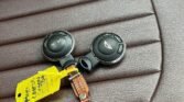 Two MINI Cooper car key fobs with a mustard yellow plastic tag and a brown braided leather keychain rest on a brown, leather car seat with vertical stitching. The key fobs feature buttons for locking, unlocking, and opening the trunk.