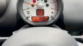 A close-up image of a MINI's dashboard and speedometer. The speedometer has a white face with markings in black and red, showing a speed of 0 mph. An orange digital display below shows "000.8 miles" for the trip and "059796 miles" for the odometer. The steering wheel is visible at the bottom.