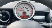 The image showcases the dashboard of a MINI, featuring a central speedometer displaying various warning lights and digital information. It includes a temperature of 11.5°C, the time of 3:18 PM, 57 miles remaining in the fuel tank, and an odometer reading of 67977 miles.