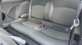 The image shows the back seats of a compact MINI car. The seats are black with a mix of smooth and patterned fabric on the seatbacks and cushions. The middle seat has a red seatbelt buckle, and there are three headrests. The car door panel is partially visible with a speaker embedded in it.