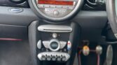 The interior of the car, particularly its dashboard and center console, exudes a sleek design reminiscent of a MINI. The dashboard features a large circular speedometer. Below it are various controls, including a digital display and a row of buttons. The manual gear stick sits in the foreground with cupholders nearby.