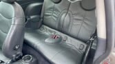 The image shows the interior of a MINI with black leather seats. The backseat has a sleek, modern design with a center armrest and cup holder. The front passenger seat and door are also visible. The floor appears clean, and there's a "no smoking" sticker on the interior door panel.