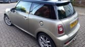 A silver MINI Cooper with a sunroof parked on a cobblestone driveway. The car has a black roof and silver alloy wheels. The license plate reads "CP55 XMA." The background includes another parked vehicle on the left and a brick wall with greenery to the right.