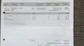 An invoice from Scotthall Ruislip for a new vehicle purchase. It includes details like customer and dealer information, vehicle price, model (Blue Metallic MINI 118i), additional options, discounts, VAT, and total cost (£20062.50). A signature is at the bottom. The background is a gray fabric.