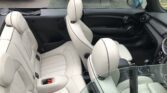 A close-up view of the interior of a MINI convertible with beige leather seats. The image shows two front seats and two smaller rear seats. The car's top is down, revealing a clear view of the seating arrangement and dashboard. A parked car with the license plate "LD07 RXM" is seen in the background.
