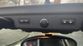 Interior view of a MINI showing the overhead console. The console contains a control panel with a circular indicator labeled "PASS AIR BAG OFF" in the center, flanked by two buttons on each side. Below the console, the rearview mirror is partially visible. A cloudy sky is seen through the windows.