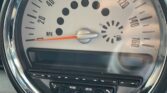 The image displays the speedometer and surrounding controls of a MINI Cooper vehicle. The analog speedometer shows a maximum speed of 150 mph, with the needle pointing at 0 mph. Beneath the speedometer are buttons labeled "MODE" and "MENU". The fuel gauge is also visible within the speedometer.