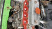 An image of an old, partially disassembled engine in the engine bay of a green MINI. The engine has exposed components, some rust, and a red engine block. Various pipes and parts are visible, with some bolts and screws missing. The car’s paint is chipped in areas around the engine bay.