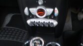 A car's central console featuring an automatic climate control display showing a temperature of 25°C, reminiscent of the classic MINI design. The console has various buttons and dials for climate control, with a row of toggle switches below it. A six-speed manual gearstick is in the foreground, indicating gears from 1 to 6 and a reverse.