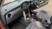 Interior of a right-hand drive mini car with a grey and black dashboard, circular air vents, manual gear stick featuring a Union Jack graphic, and two-tone fabric seats. The door is open, and the car is parked on concrete outdoors—perfect for any mini trader.
