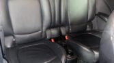 The image shows the black leather rear seats of a mini car, featuring two separate seatbacks with headrests and a small center console with cup holders. The interior appears clean and well-maintained, with part of the front seat and door visible.