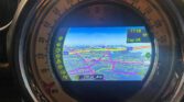 A close-up of a MINI car's dashboard display shows a GPS navigation map with colorful routes, street names, and the time 17:18. The outer ring features a speedometer in MPH, and the map highlights roads, points of interest, and directions in Cap UK.