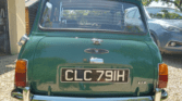 A green vintage mini car is parked outdoors on a gravel driveway. The photo shows the rear view with a black license plate "CLC 791H," chrome bumpers, red rear lights, and a sunny background with trees.