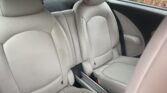 The image shows the back seat of a mini car with two light gray leather seats, separated by a small center console. The seats have rounded headrests. Through the window, green bushes and red leaves are visible outside.