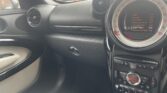 The photo shows the front passenger side of a mini car interior, including the dashboard, air vents, glovebox, cream and black door, cream seat, and the central speedometer display showing radio station options and DAB menu with orange accents.