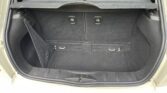 Open trunk of a mini car with black carpeted interior, foldable rear seats, a net storage compartment on the left side, and two metal hooks on the floor. The hatchback door is open, revealing the rear seatbacks and headrests.