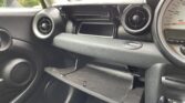 The image shows the interior of a mini car, focusing on the passenger side. Both the glove compartment and a storage compartment above it are open. The dashboard, air vents, and part of the speedometer are also visible.