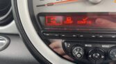 Close-up of a MINI car dashboard display showing options: "TEL" with a phone icon, "COMP," and "CONFIG." Below are buttons and dials for audio and menu functions. Part of the speedometer is visible above the display. Perfect for any MINI trader.